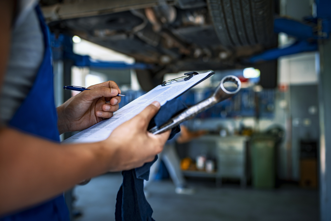Unrecognizable Male mechanic under car preparing checklist in workshop. Photo of mechanic taking notes under a car.
